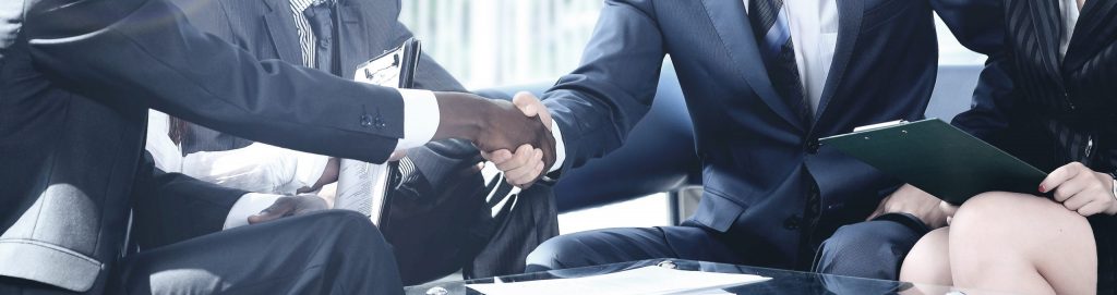 Sharply dressed business lawyers with clients in conference room, finishing up a business meeting by shaking hands.
