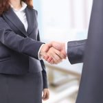 Male and female lawyer well dressed in dark grey business suits, standing and shaking hands.
