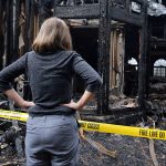 Woman with hands on her hips looking at house destroyed by fire.